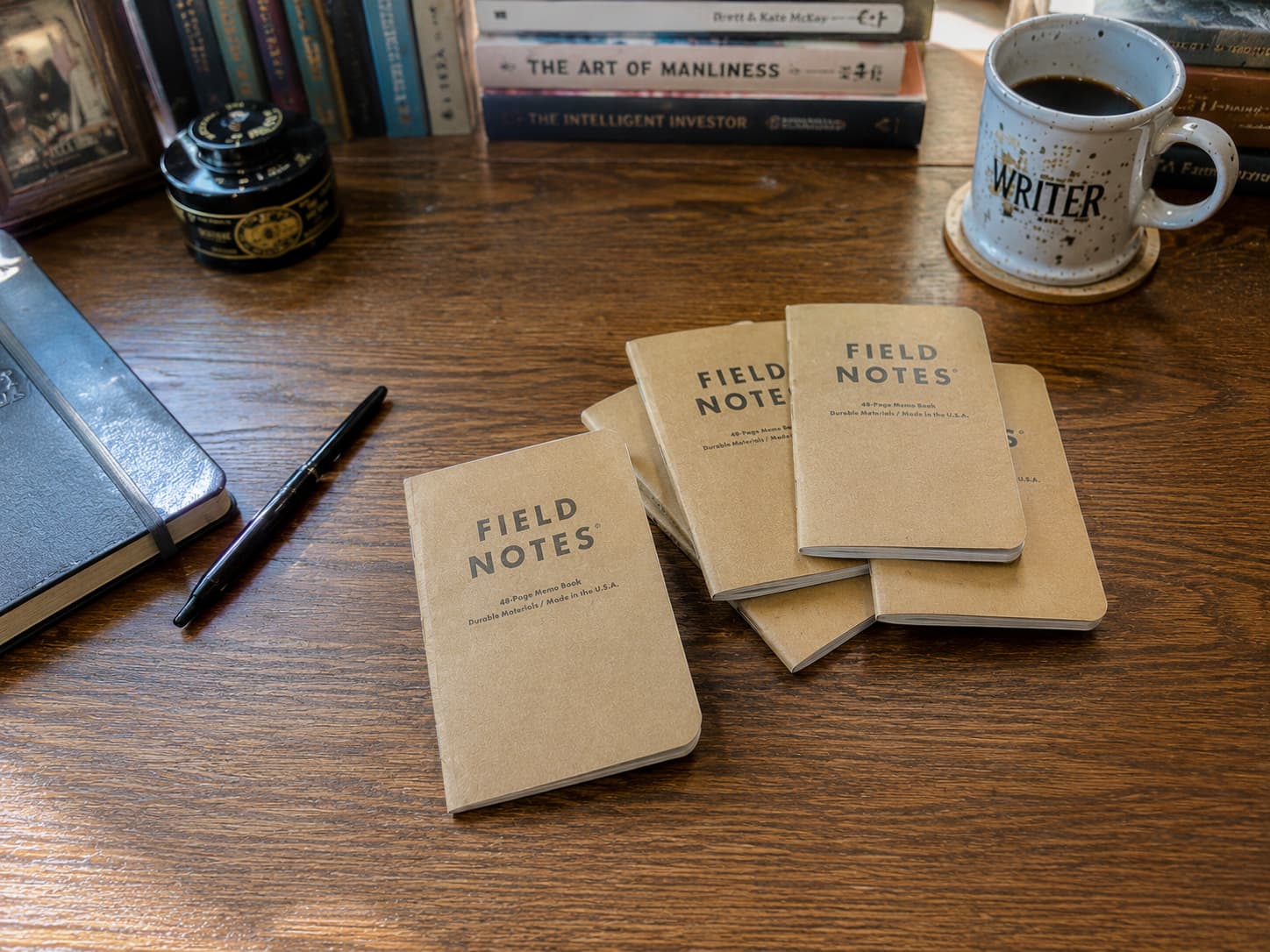 Field Notes memo books on a wooden writer desk with a pen and coffee mug