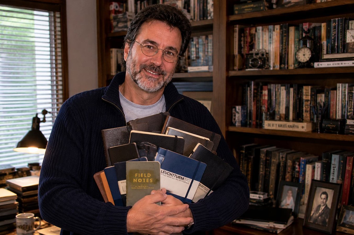 Roger Davis holding a stack of writing journals in a book-lined study